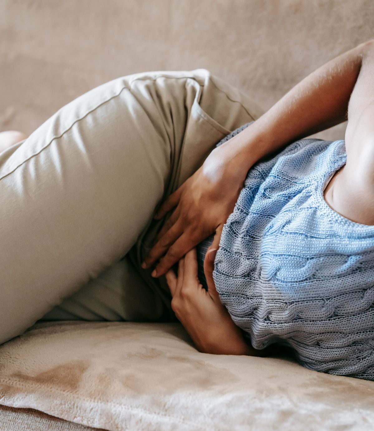 Mulher sentindo desconforto abdominal no sofá, ilustrando sintomas que não devem esperar por uma consulta marcada